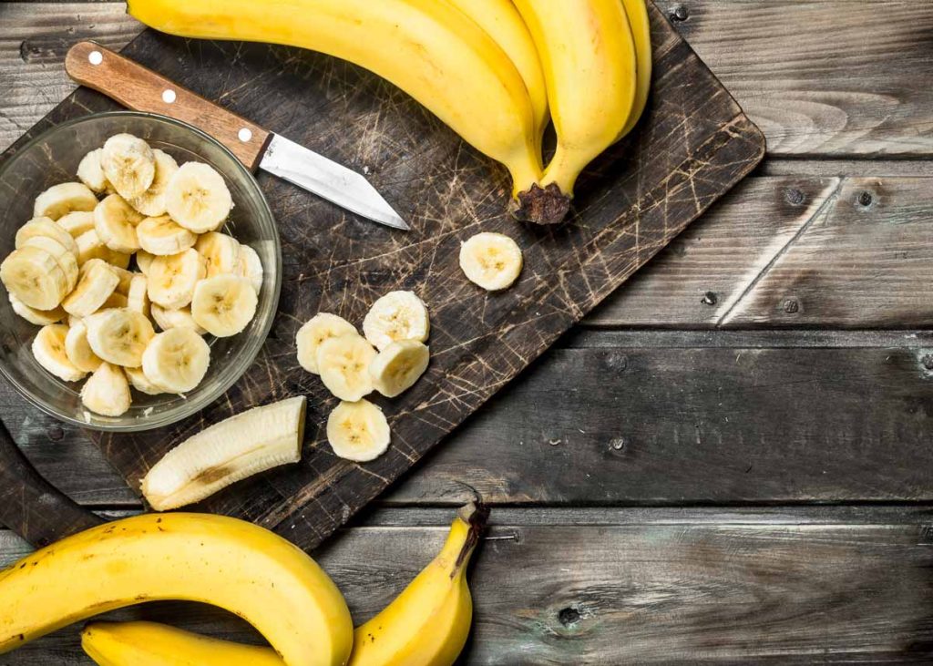 Bananas e bananas fatiadas em um prato em cima de uma tábua de corte com uma faca