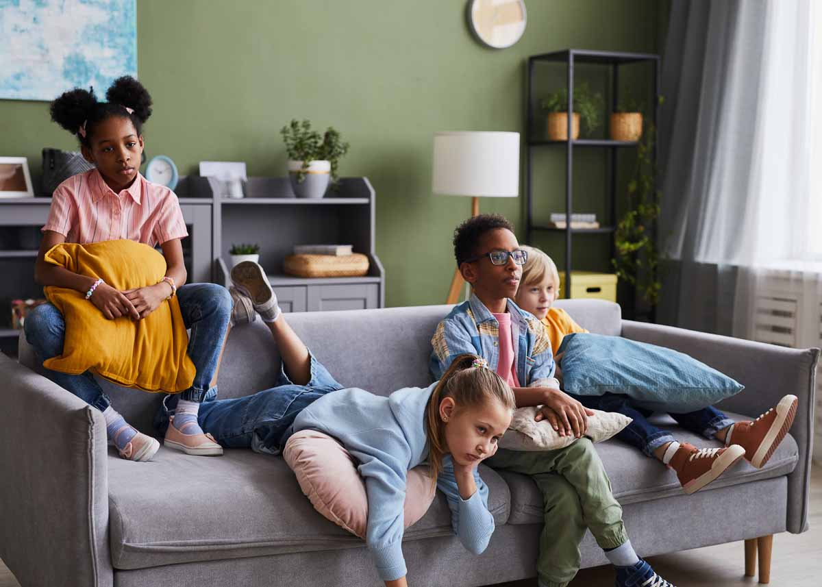 Grupo de crianças assistindo TV em casa enquanto relaxa no sofá parecendo entediados
