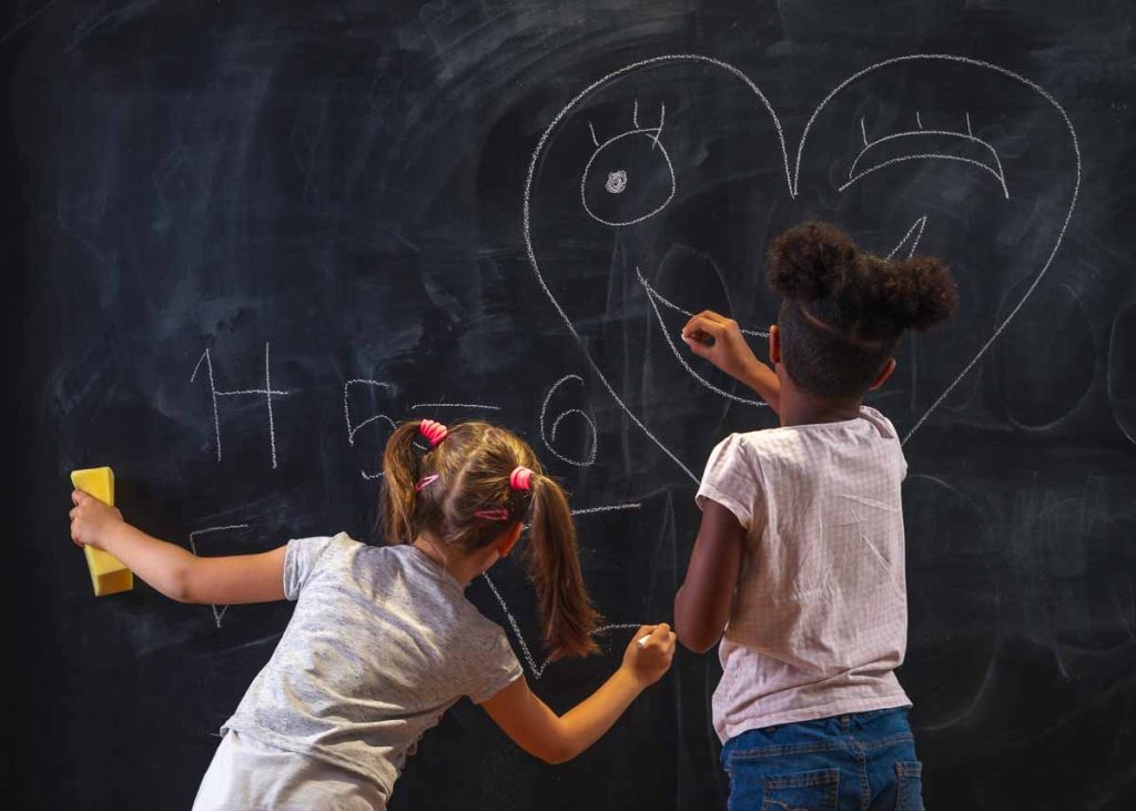Duas lindas garotinhas se divertindo desenhando em uma lousa na sala de aula no intervalo entre as aulas