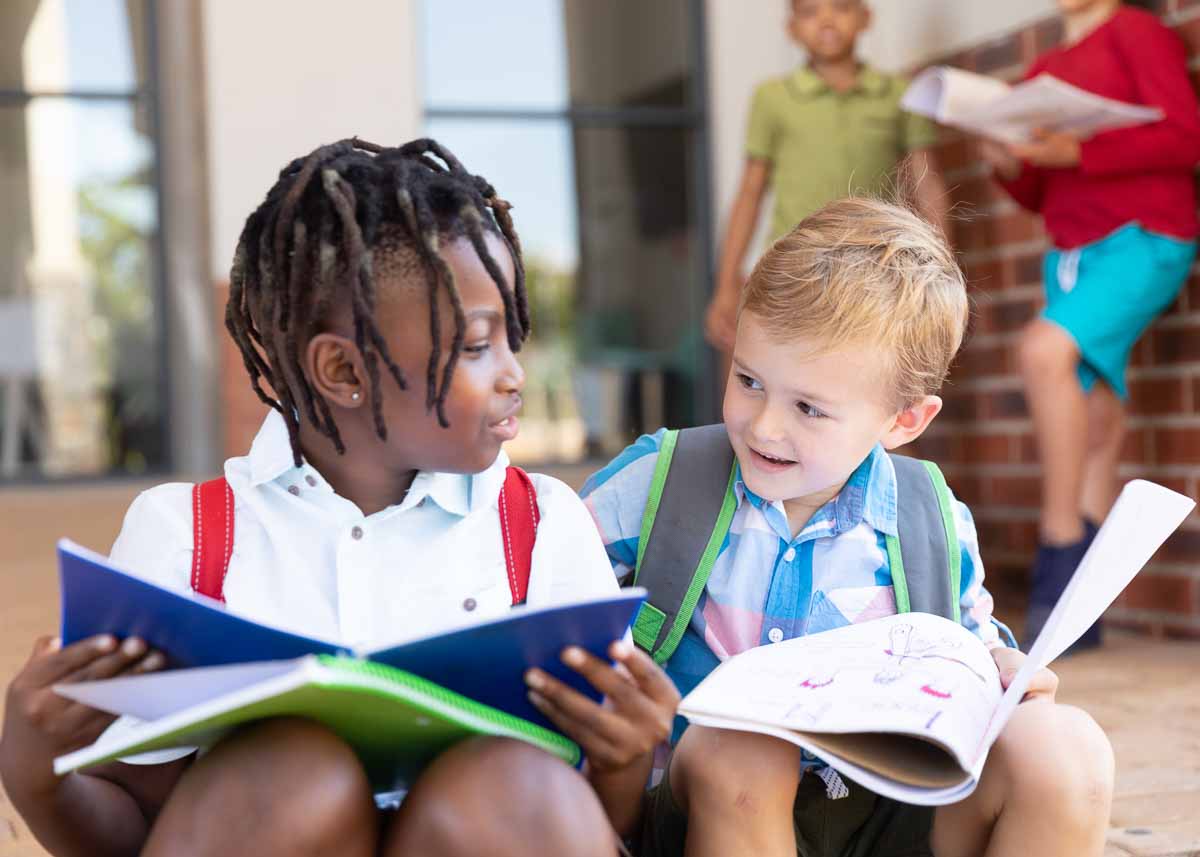 Alunos multirraciais do ensino fundamental estudando enquanto estão sentados no chão da escola. inalterado, infância, educação, aprendizagem, juntos e de volta ao conceito de escola.