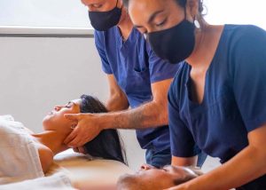 Dois massagistas fazendo massagem em um homem e uma mulher, exemplo de massoterapia, nicho do mercado de trabalho para educação física