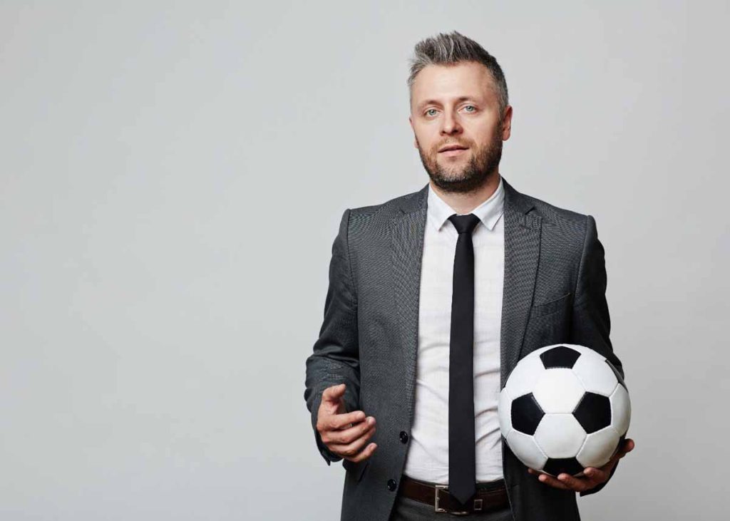 Homem de terno segurando uma bola de futebol