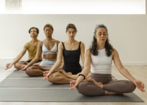 Grupo de pessoas diversas em meditação, praticando yogaterapia em um estúdio contemporâneo.